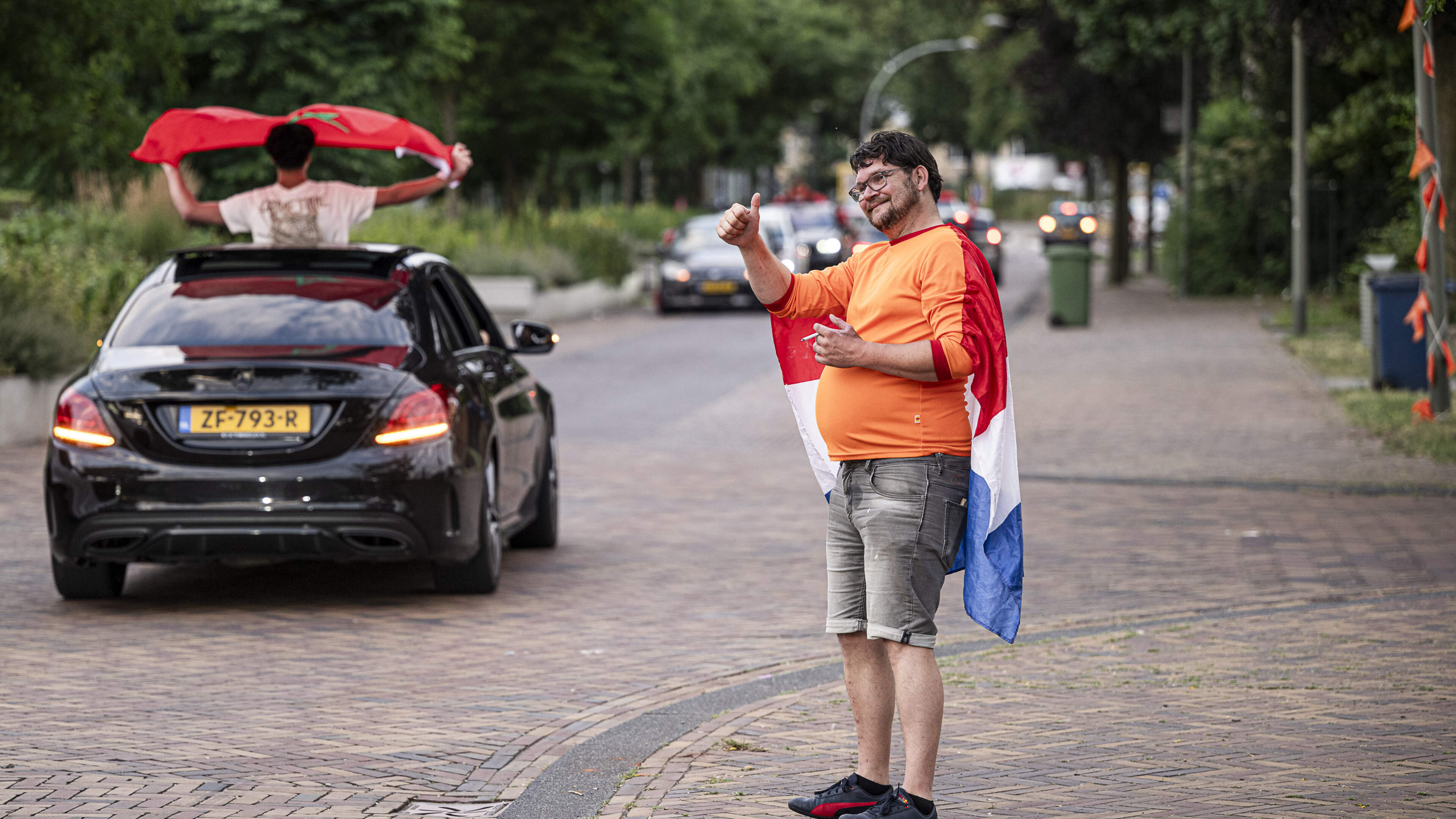 Terwijl de Marokkanen toeterend langsrijden, staan Oranjefans langs de kant te klappen